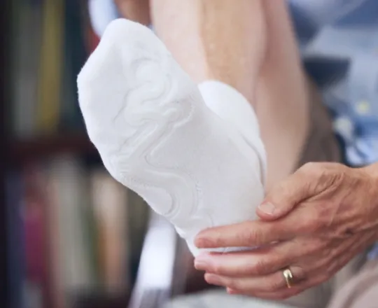 Close-up of a person putting on a white sock on their foot while sitting down.