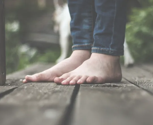 Bare feet of a person standing on a wooden surface wearing rolled-up jeans.