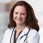 Smiling female doctor with curly brown hair wearing a white coat and stethoscope.