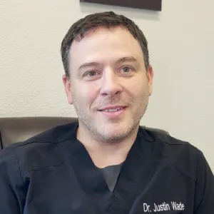 Portrait of a smiling man wearing a black medical scrub top embroidered with 'Dr. Justin Wade'.