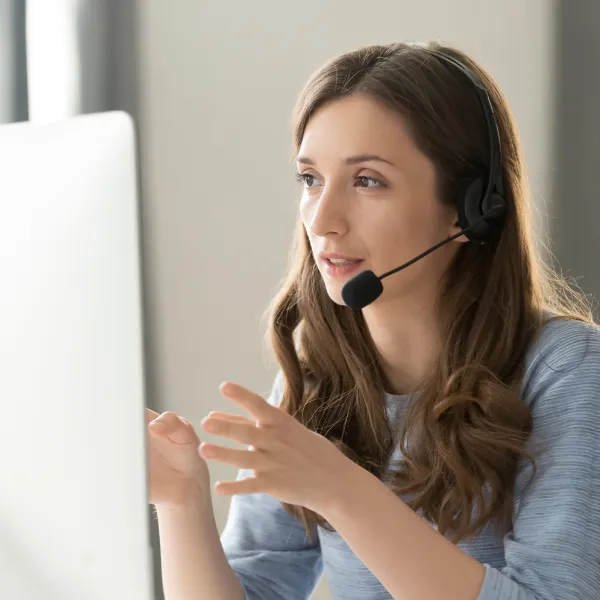 Woman with long brown hair wearing a headset and gesturing while looking at a computer screen.