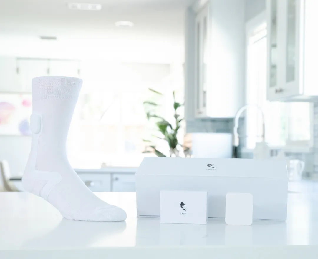 White smart sock on a white surface next to a white box and small cards, set in a bright kitchen.
